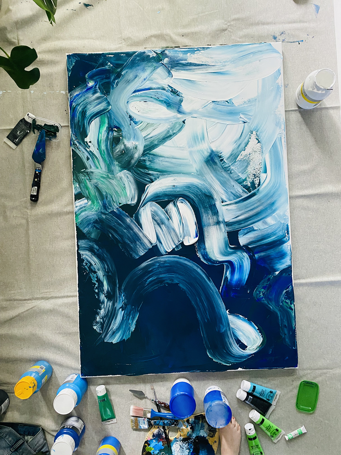 Blue and white abstract painting in progress with art supplies