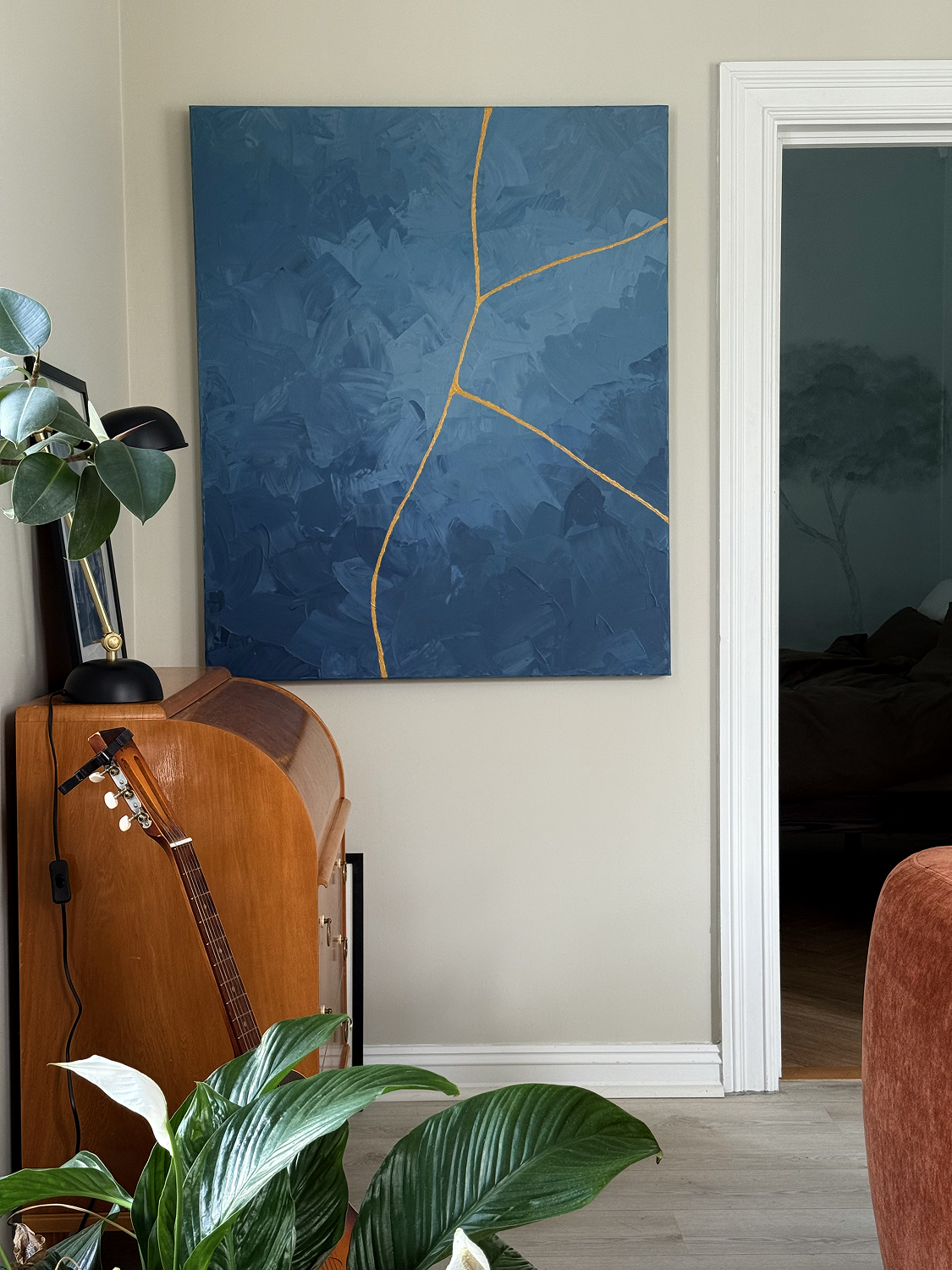 Abstract blue painting with gold kintsugi-style lines displayed in home interior